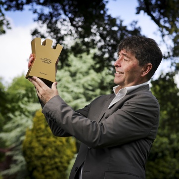 Michael Crummey holding the gold coloured winning trophy outside in the park.