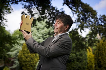 Michael Crummey holding the gold coloured winning trophy outside in the park.