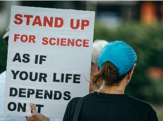 A photo of someone at a protest holding a sign that reads stand up for science as if your life depends on it