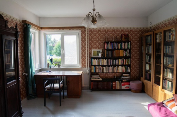 a room with patterned red wallpaper, and bookshelves. there is a writing desk under a window.
